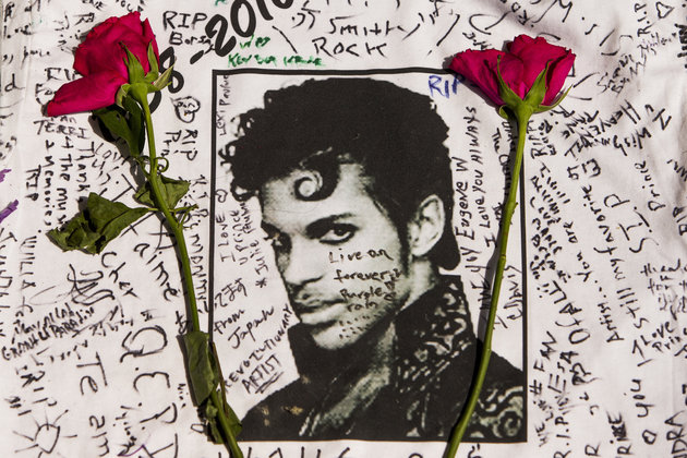 Flowers lay on a T-shirt signed by fans of singer Prince at a makeshift memorial place created outside Apollo Theatre in New York, Friday, April 22, 2016.